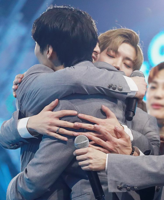 NU'EST members hug each other at the final evaluation of Produce 101 season 2